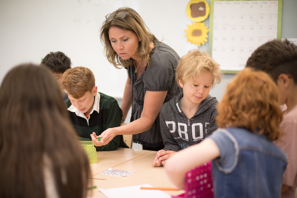Kvinnlig lärare som hjälper elever vid ett bord.